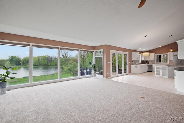 unfurnished living room with a water view, vaulted ceiling, light colored carpet, a ceiling fan, and light tile patterned flooring