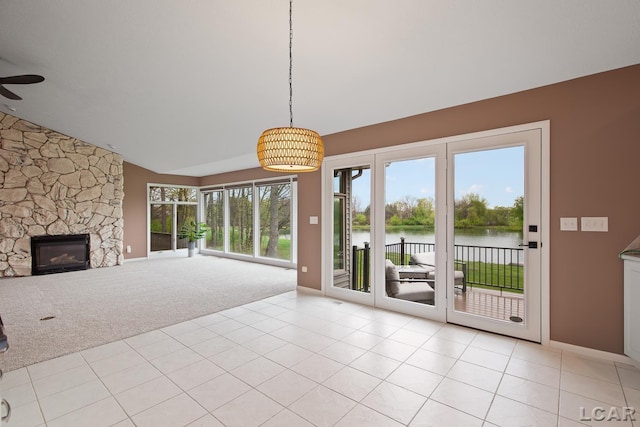 unfurnished living room with a water view, light colored carpet, vaulted ceiling, a fireplace, and plenty of natural light