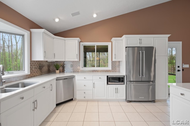 kitchen with appliances with stainless steel finishes, lofted ceiling, decorative backsplash, light countertops, and plenty of natural light