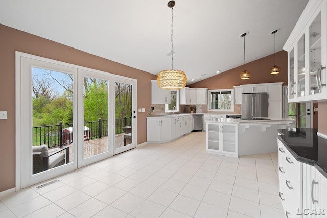 kitchen featuring stainless steel appliances, vaulted ceiling, a sink, tasteful backsplash, and glass insert cabinets