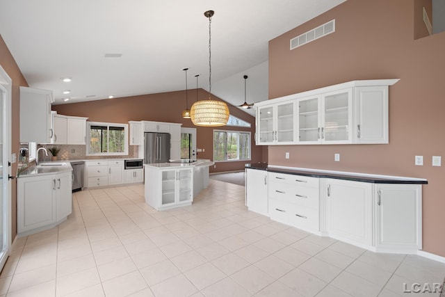kitchen with appliances with stainless steel finishes, glass insert cabinets, decorative backsplash, white cabinetry, and hanging light fixtures