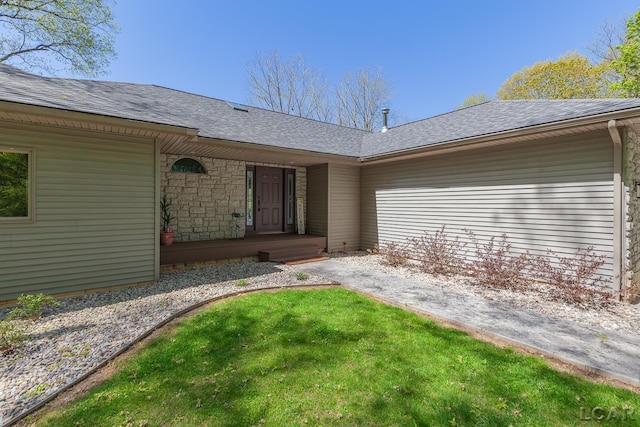 view of exterior entry with a shingled roof and a yard