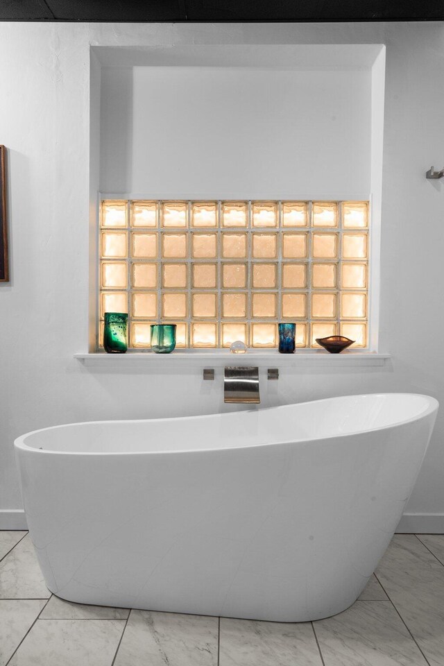 full bath with marble look tile flooring, a soaking tub, and baseboards
