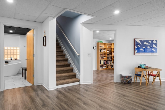 stairway with wood finished floors, baseboards, and a drop ceiling