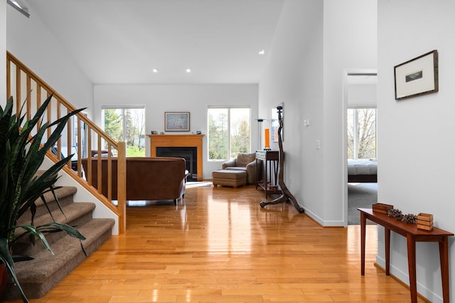 living area with stairs, recessed lighting, light wood-style floors, a fireplace, and a high ceiling
