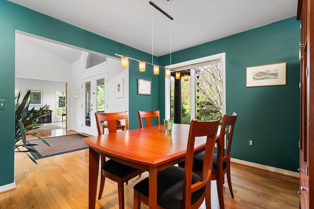 dining space featuring light wood-style floors, vaulted ceiling, baseboards, and french doors