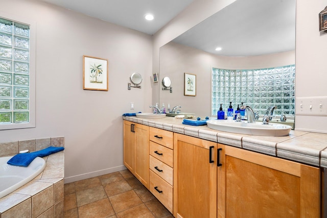 full bath with double vanity, a relaxing tiled tub, plenty of natural light, baseboards, and recessed lighting