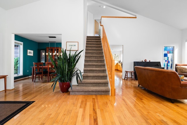 stairs with high vaulted ceiling, hardwood / wood-style floors, and a chandelier