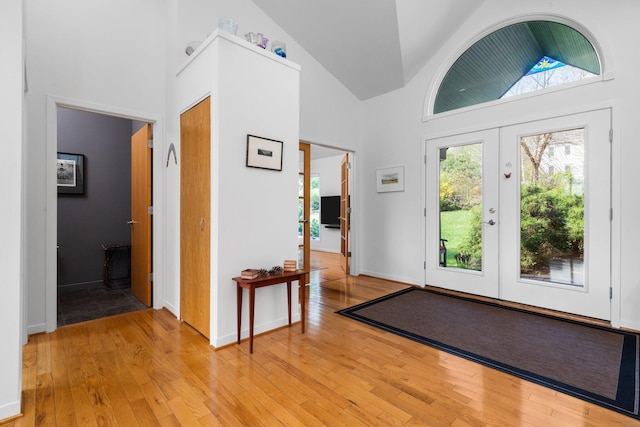 foyer entrance with light wood-style floors, high vaulted ceiling, baseboards, and french doors