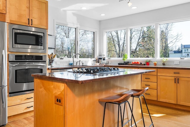 kitchen featuring stainless steel appliances, a center island, a kitchen bar, light wood-type flooring, and a sink