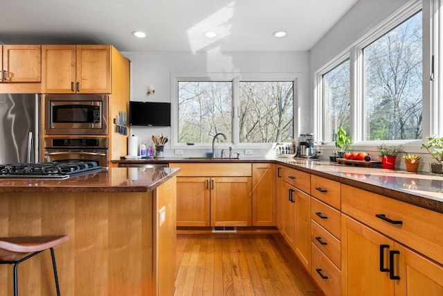 kitchen featuring appliances with stainless steel finishes, a sink, dark stone countertops, light wood-style flooring, and recessed lighting