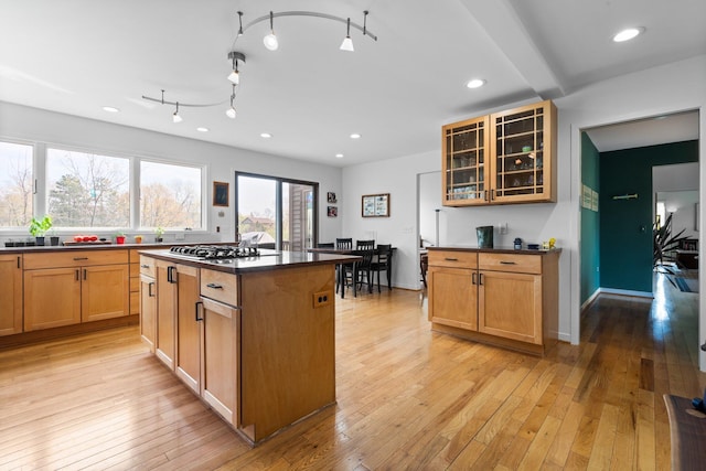 kitchen featuring dark countertops, a kitchen island, glass insert cabinets, light wood finished floors, and recessed lighting