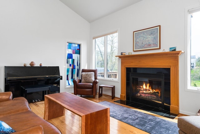 living area with a fireplace with flush hearth, lofted ceiling, hardwood / wood-style floors, and baseboards