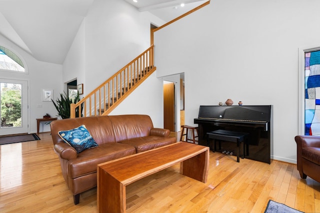 living room featuring high vaulted ceiling, light wood-style floors, and stairs