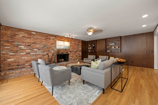 living area with a ceiling fan, light wood-type flooring, a fireplace, brick wall, and wooden walls