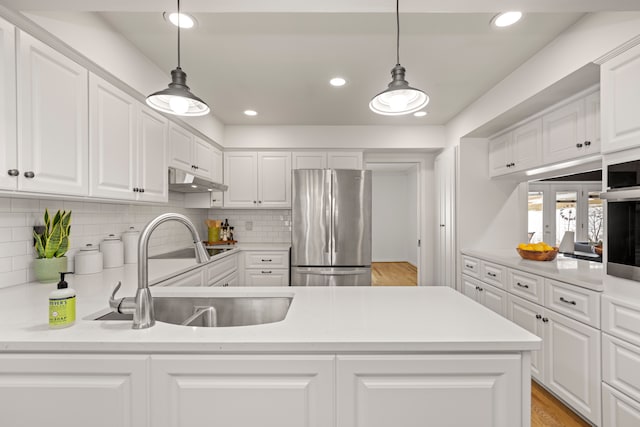 kitchen with stainless steel appliances, a sink, under cabinet range hood, white cabinetry, and light countertops
