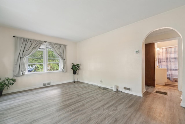 empty room featuring arched walkways, wood finished floors, and baseboards