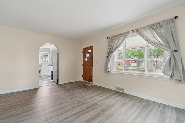 unfurnished living room with wood finished floors, plenty of natural light, arched walkways, and baseboards