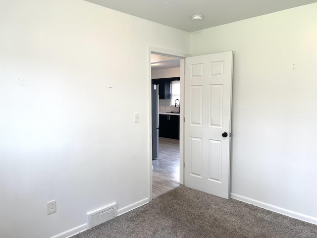 carpeted empty room with a smoke detector, baseboards, and a sink