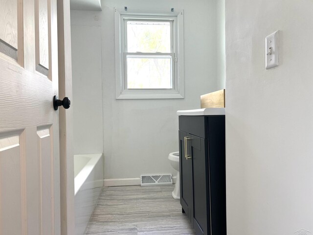 bathroom with toilet, vanity, baseboards, a tub, and wood finished floors