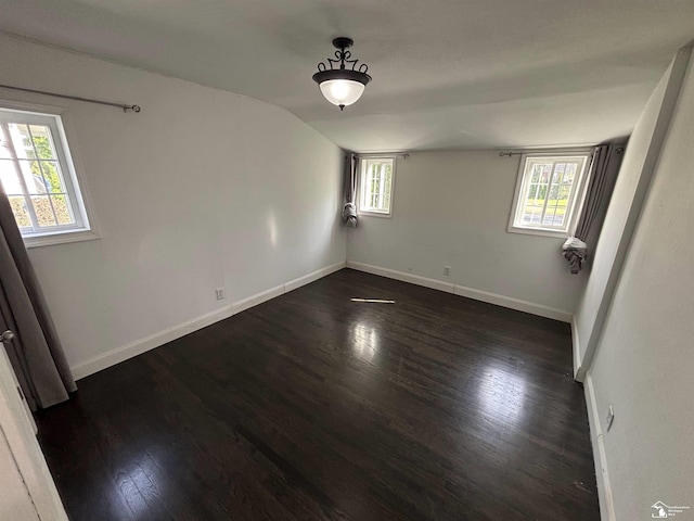 unfurnished room featuring dark wood finished floors, healthy amount of natural light, baseboards, and vaulted ceiling
