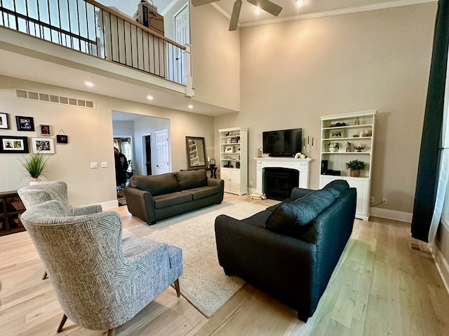 living room featuring ornamental molding, ceiling fan, a high ceiling, a fireplace, and wood finished floors