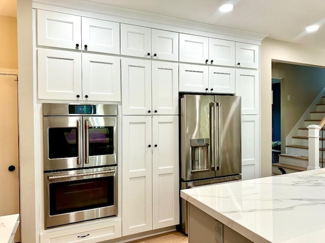 kitchen featuring appliances with stainless steel finishes, light stone counters, white cabinets, and recessed lighting