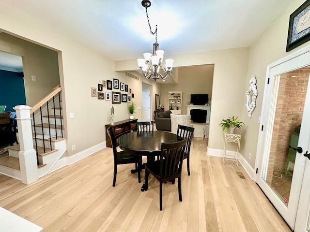 dining area featuring light wood-type flooring, a chandelier, baseboards, stairs, and a fireplace