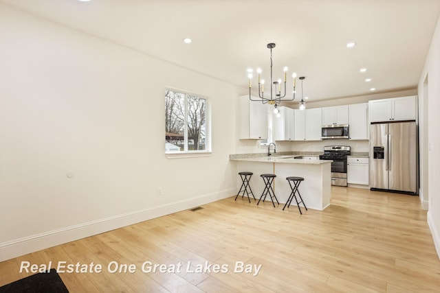 kitchen featuring appliances with stainless steel finishes, a chandelier, baseboards, a sink, and a breakfast bar area
