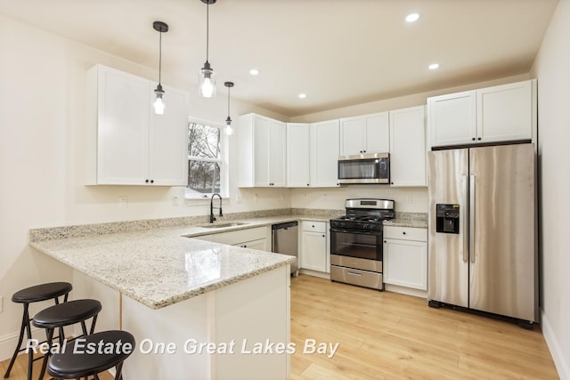 kitchen featuring appliances with stainless steel finishes, a sink, a peninsula, white cabinetry, and light stone countertops
