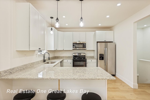 kitchen featuring appliances with stainless steel finishes, a sink, light wood-type flooring, light stone countertops, and a peninsula