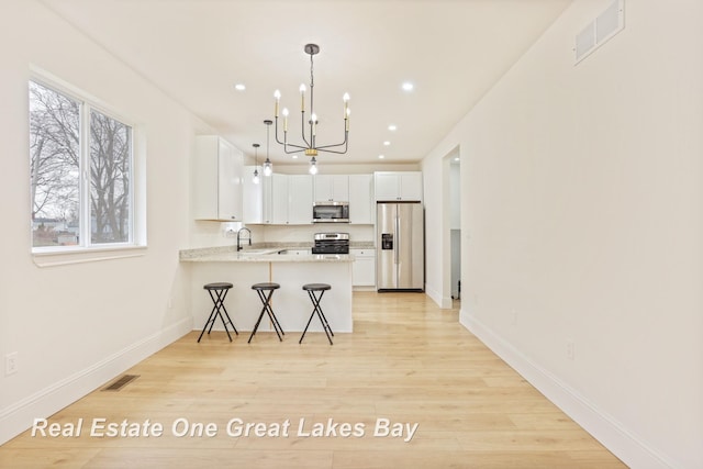kitchen with appliances with stainless steel finishes, a sink, a chandelier, a peninsula, and light wood-style flooring