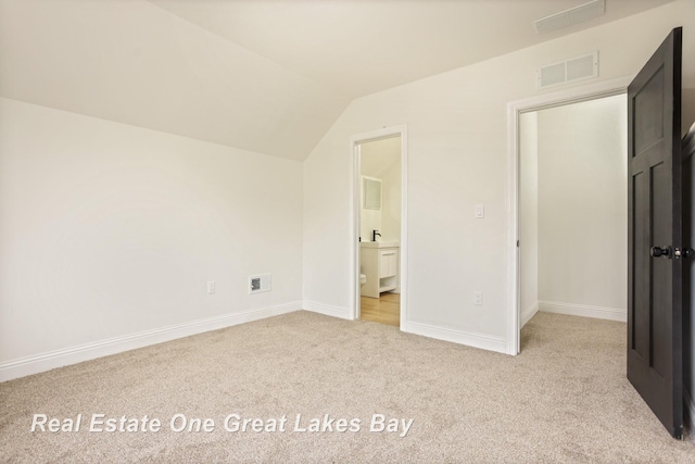 unfurnished bedroom featuring carpet flooring, lofted ceiling, baseboards, and ensuite bathroom