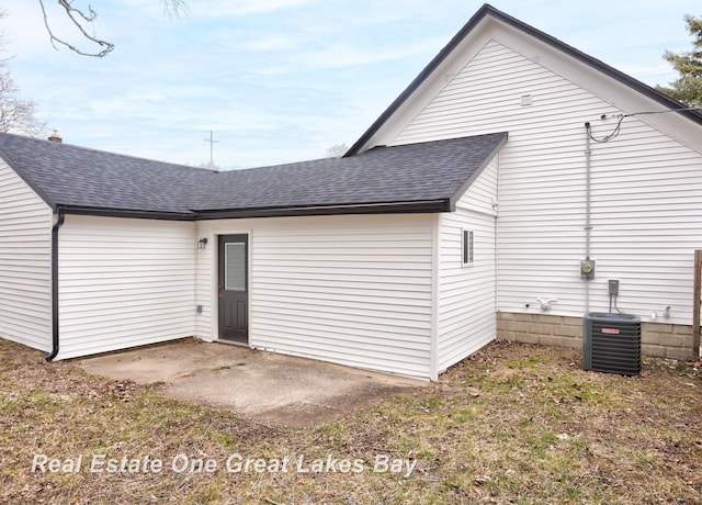 rear view of house with central air condition unit, roof with shingles, and a patio