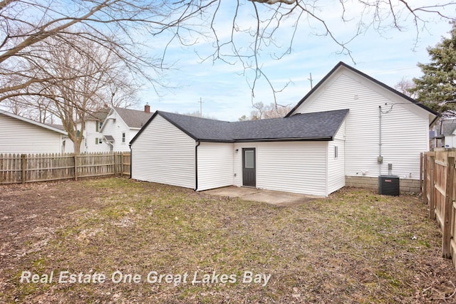 rear view of property with a fenced backyard, roof with shingles, and central AC
