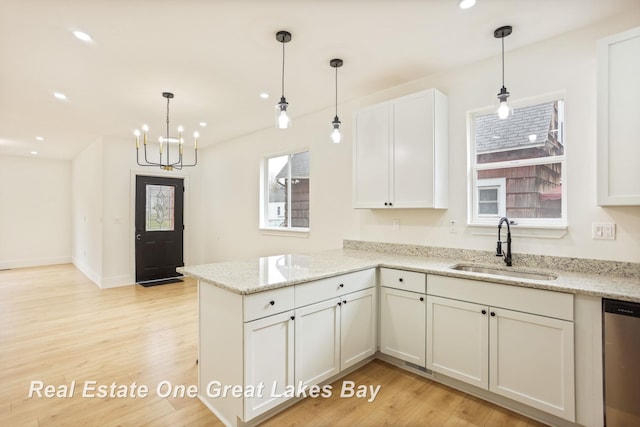 kitchen with a sink, dishwasher, a peninsula, light wood-type flooring, and a chandelier