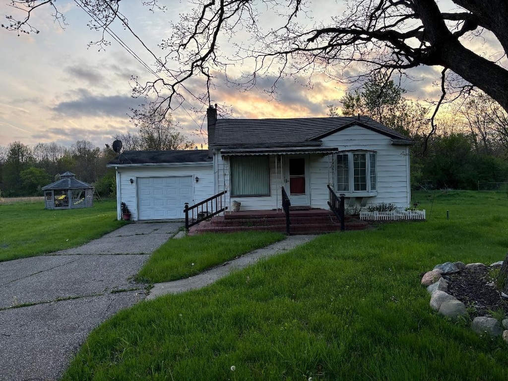 bungalow-style house with an attached garage, a yard, a chimney, driveway, and a gazebo