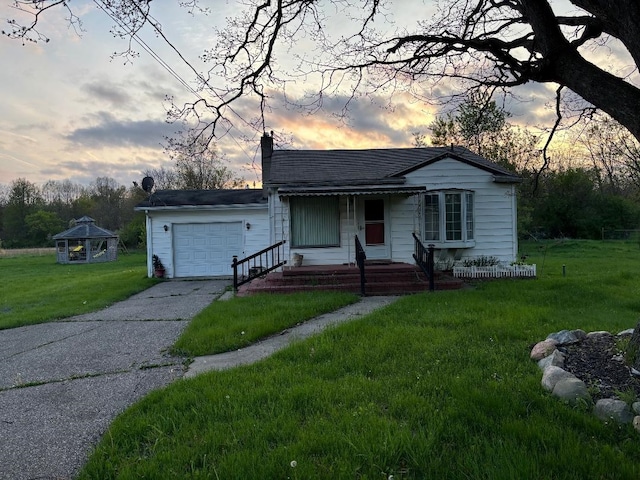 bungalow-style house with an attached garage, a yard, a chimney, driveway, and a gazebo