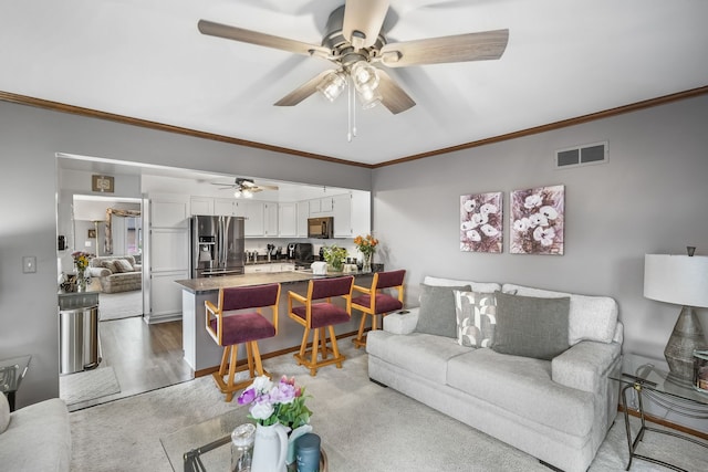 living area with crown molding, a ceiling fan, and light wood-style floors