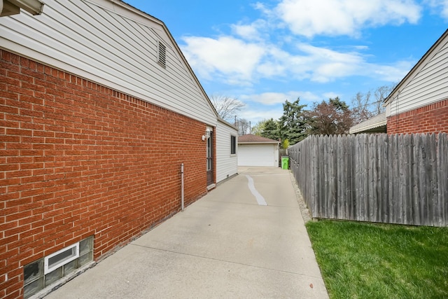 view of side of home with fence, brick siding, a detached garage, and an outbuilding