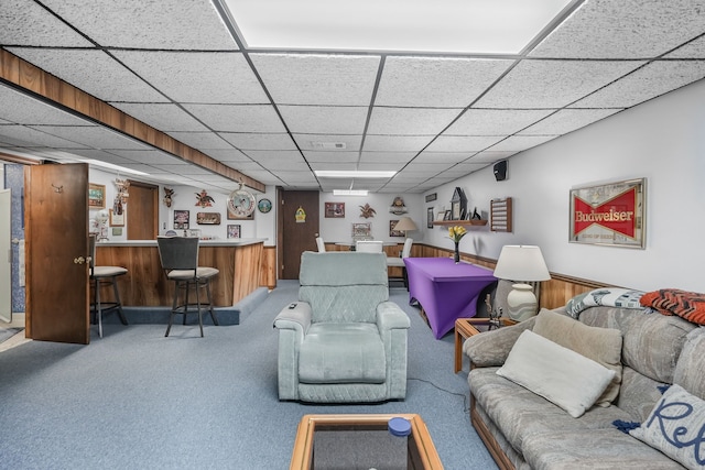 living room featuring bar area, carpet flooring, a drop ceiling, and wood walls