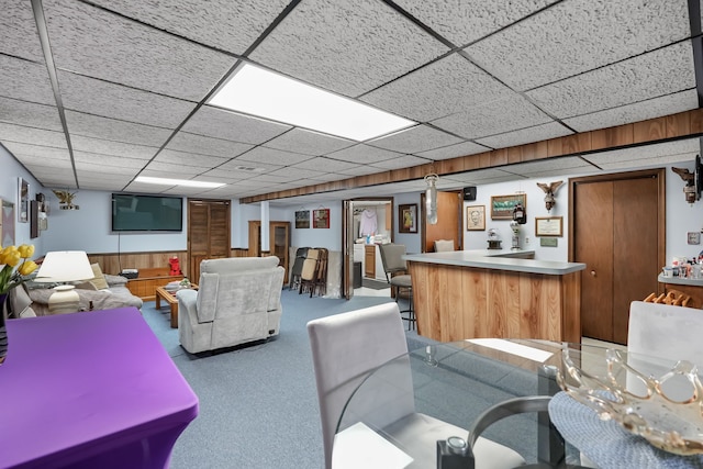 living area featuring bar area, a drop ceiling, and wooden walls