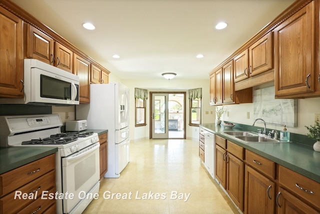kitchen featuring white appliances, a sink, dark countertops, brown cabinetry, and recessed lighting