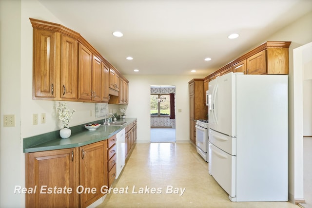 kitchen with white appliances, a sink, recessed lighting, brown cabinetry, and dark countertops