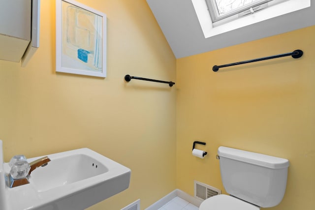 bathroom featuring lofted ceiling, toilet, a sink, a skylight, and tile patterned floors