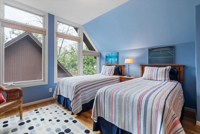 bedroom with multiple windows, vaulted ceiling, wood finished floors, and baseboards