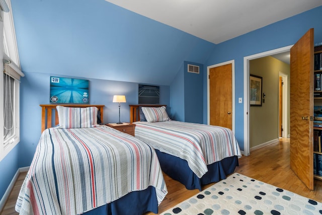 bedroom with vaulted ceiling, wood finished floors, and baseboards