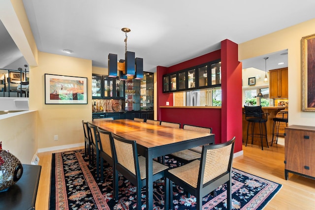 dining area featuring light wood-style flooring, bar, and baseboards