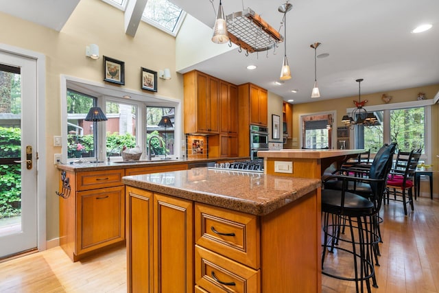 kitchen featuring a sink, a kitchen island, brown cabinetry, a breakfast bar area, and a skylight