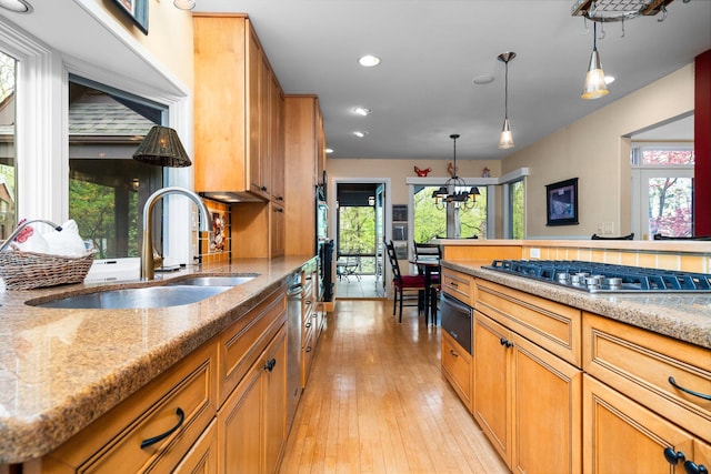 kitchen featuring a sink, a warming drawer, stainless steel gas stovetop, light stone counters, and light wood-style flooring